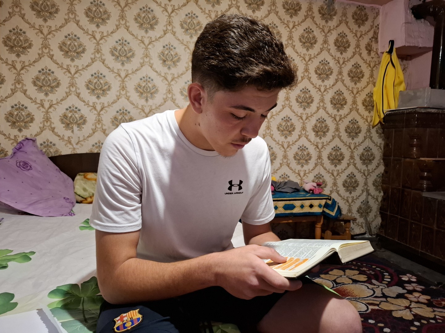 A boy sitting on the bed reading his bible