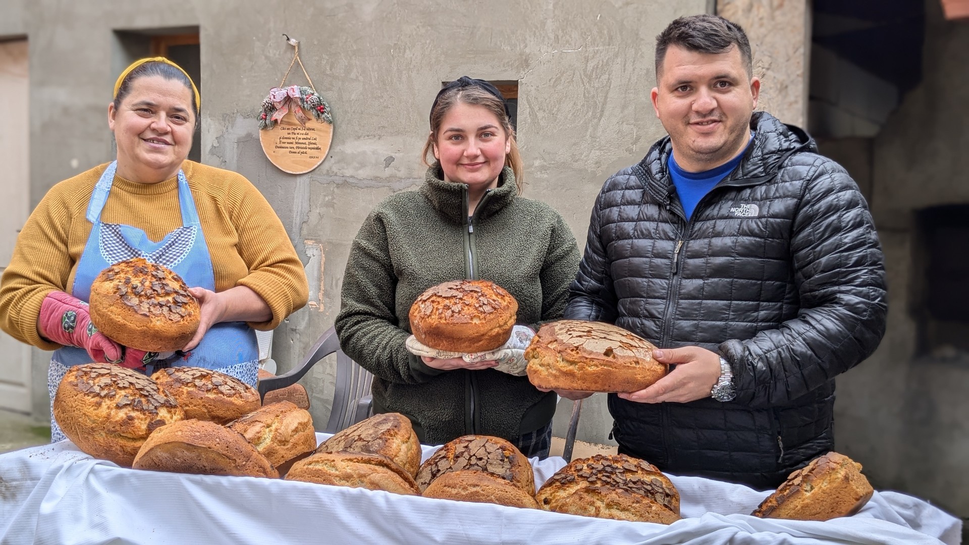 Three people holding some of the finished loaves of bread.