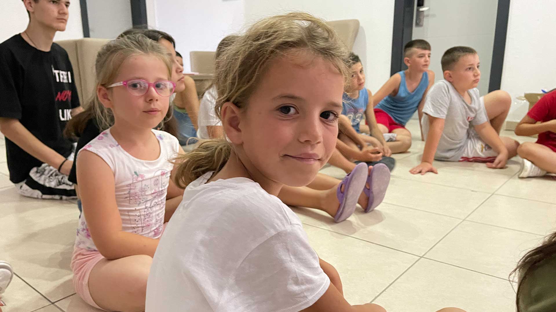 Children sit listening to a talk at a summer camp.